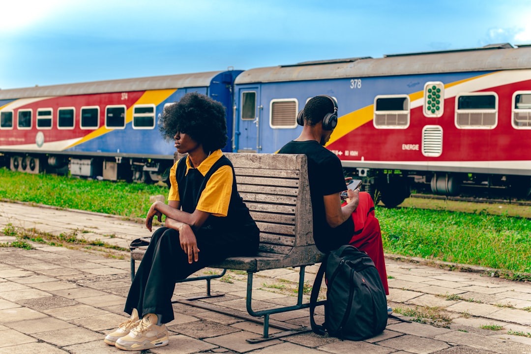 Couple on train platform bench with train behind them.